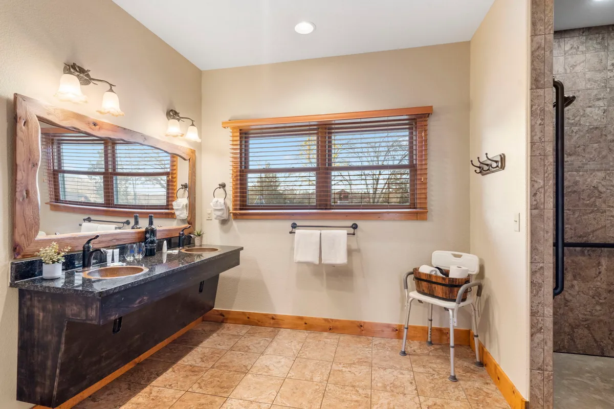 A serene ensuite bathroom with a double sink vanity, large wooden mirror, and a shower area bathed in morning light through a window. The calm atmosphere is perfect for self-care routines after a day of adventure.