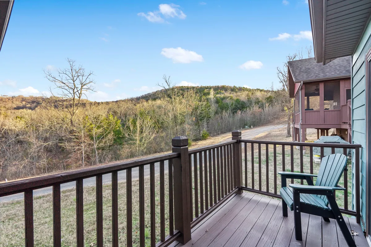 A peaceful deck scene with a green chair facing a sweeping mountain view. The deck railing frames the natural landscape, inviting guests to relax, read, or share quiet moments while soaking in the scenic beauty.