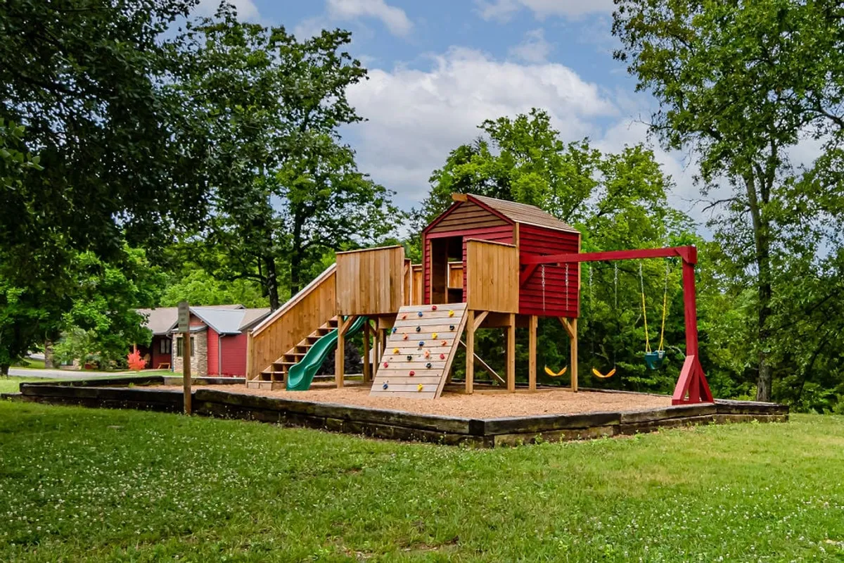 A cheerful playground area with swings, a slide, and a sturdy play structure, all surrounded by greenery. The setting is vibrant and inviting, perfect for children’s play and family picnics.