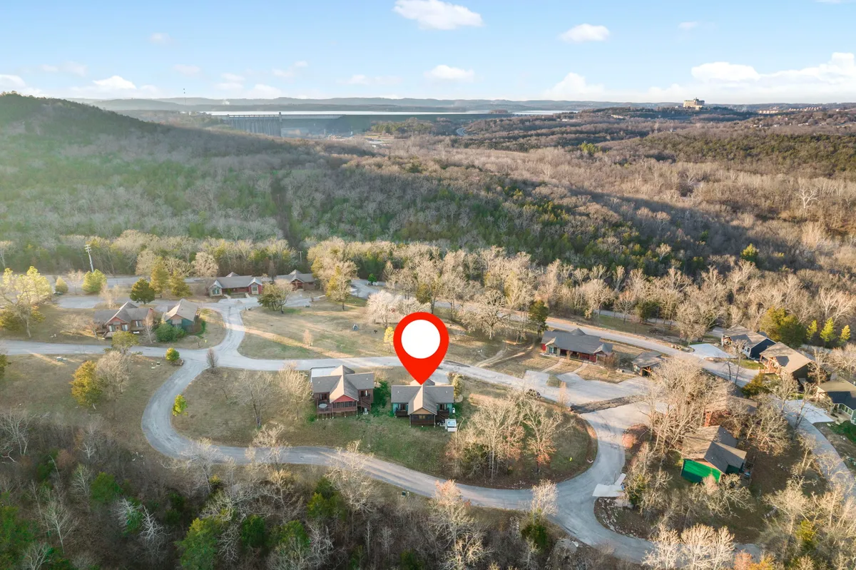 The photo captures tranquil residential homes amid lush trees, with a winding road that hints at scenic drives and easy access to nearby attractions. The peaceful setting evokes the beauty and serenity of the Ozarks environment.