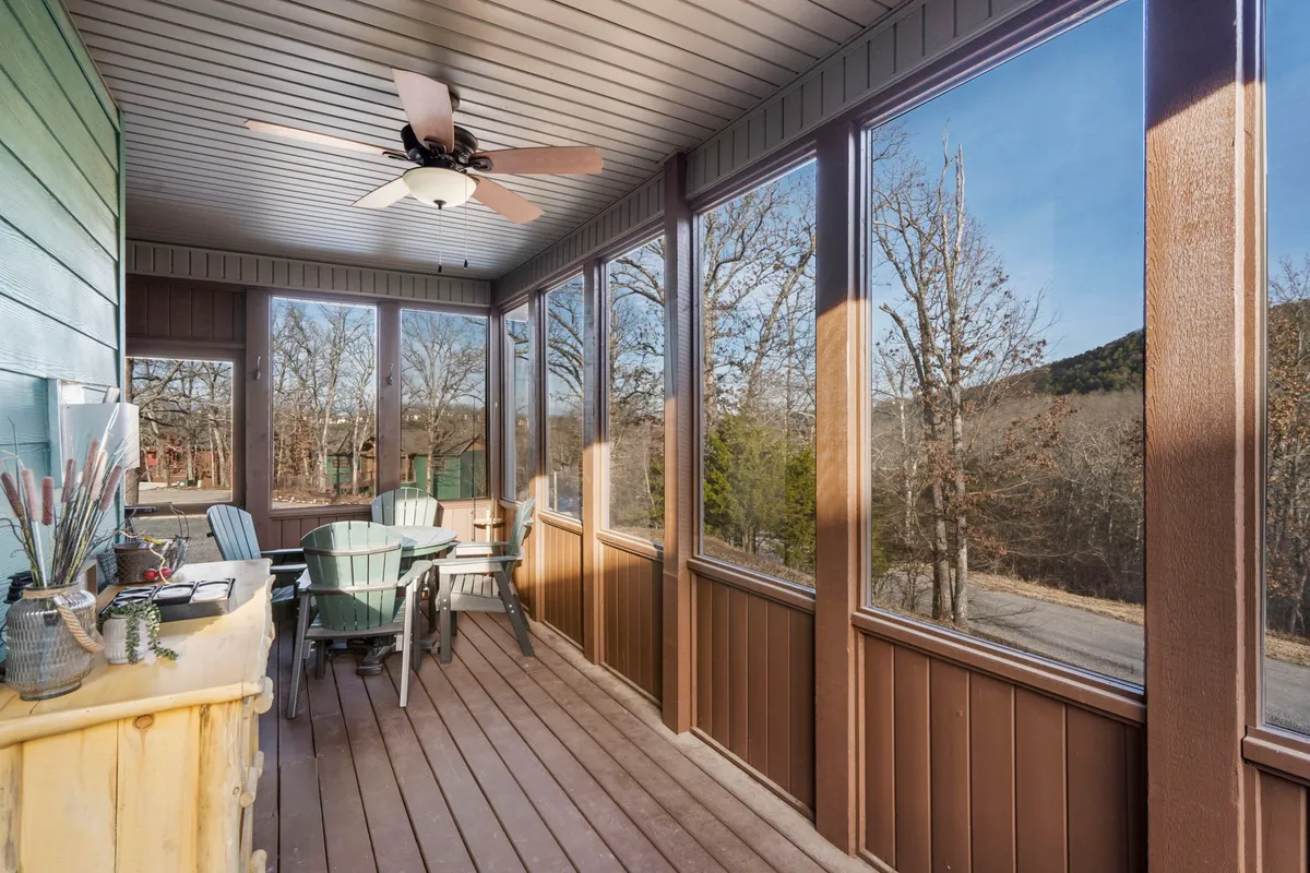 An inviting interior space featuring a dining table surrounded by Adirondack chairs, a ceiling fan overhead, and large windows offering clear sightlines to the outdoors. The room exudes a breezy, relaxed atmosphere perfect for morning coffee or quiet moments.