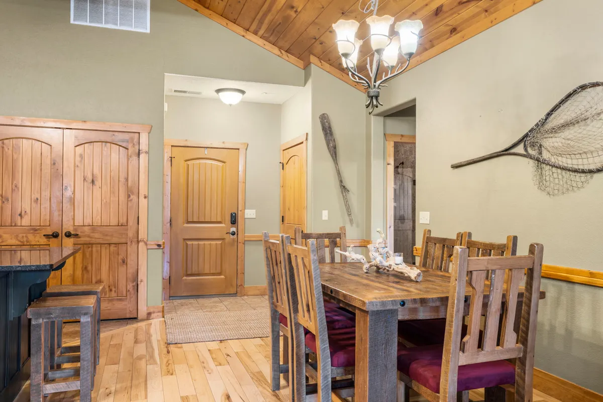 A cozy dining area with a spacious wooden table, elegant chandelier, and decorative wall art. The space is designed for family dinners, game nights, and cheerful communal gatherings, inviting guests to come together.