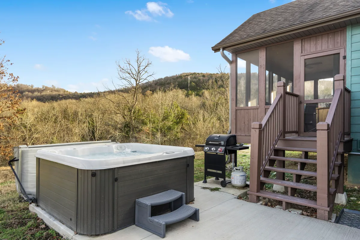 An inviting outdoor scene with a grill, screened porch, and hot tub, all set against a scenic mountain view. The grill is ready for barbecuing, and the screened porch is perfect for enjoying meals surrounded by nature.