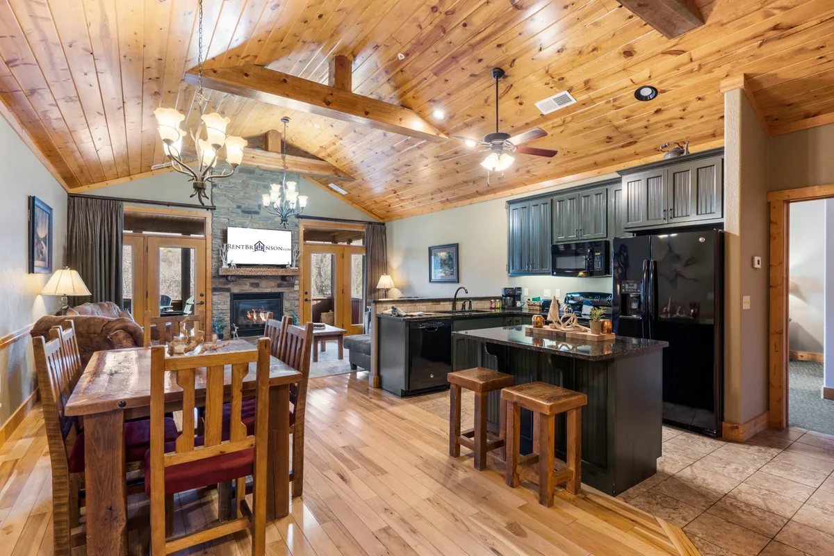 A wide view of the living area showcasing a harmonious blend of the dining table, kitchen island, fireplace, and large sunlit windows. The layout demonstrates the seamless connection between living, dining, and kitchen zones, inviting interaction and togetherness for families and friends.