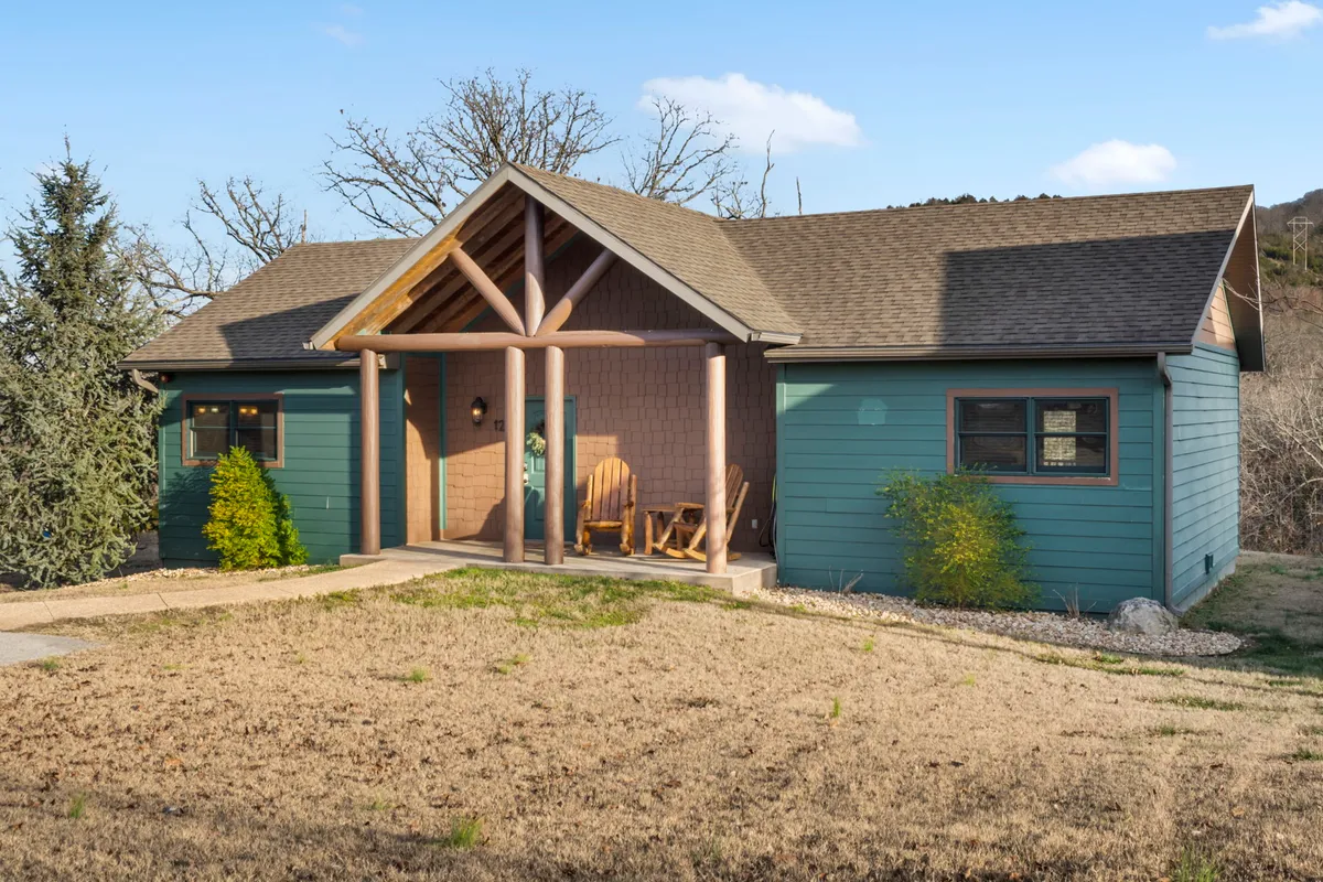 This image shows a charming front porch with wooden rocking chairs, decorative columns, and green shrubs framing the entrance. The setting exudes relaxation and offers a view of the outdoors, inviting guests to unwind and enjoy the natural beauty surrounding the lodge.