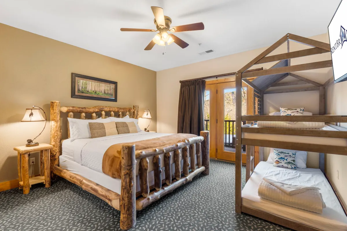 A family-friendly bedroom with both a log king bed and a bunk bed, complemented by balcony doors and cheerful artwork above the bed. The room feels inviting and offers flexible sleeping arrangements for families or small groups.